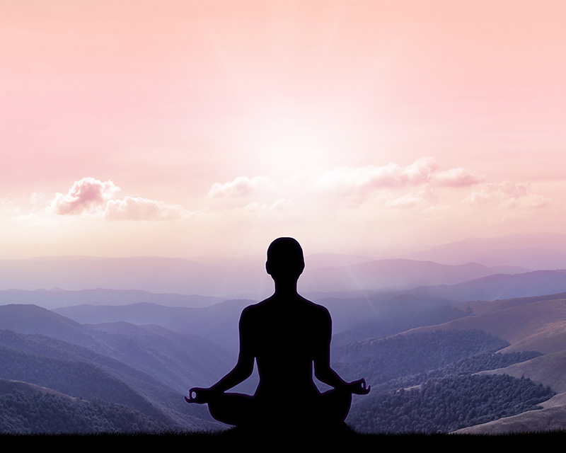 Woman meditating while looking at the mountains - integrated approach to mind and body